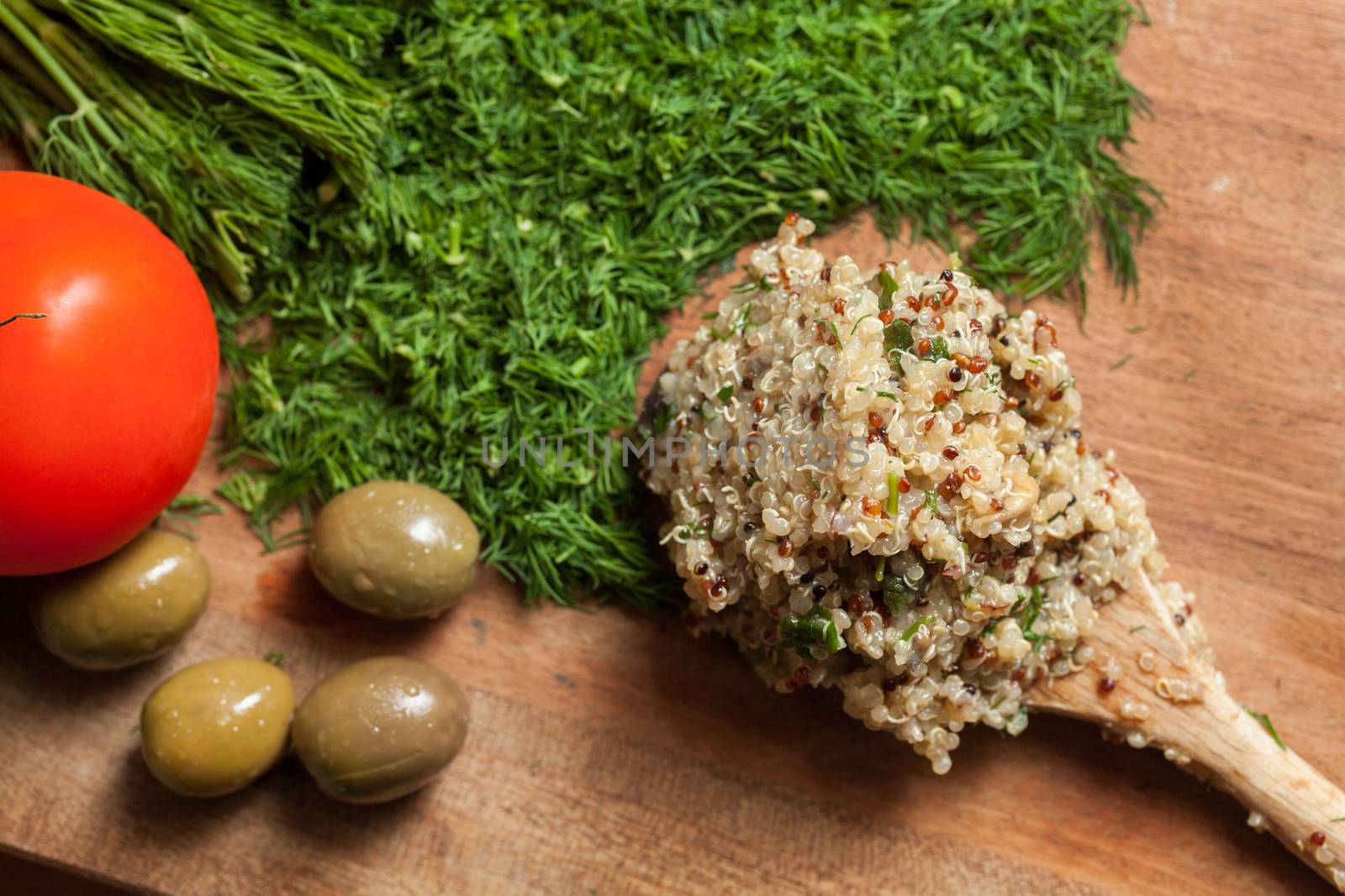 Wooden spoon with ready cooked quinoa, on a wooden surface with dill