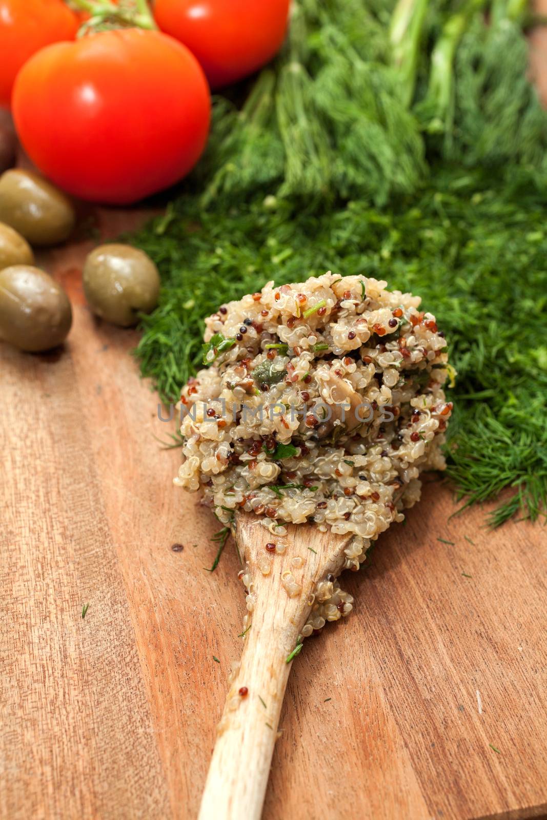 Wooden spoon with ready cooked quinoa, on a wooden surface with dill