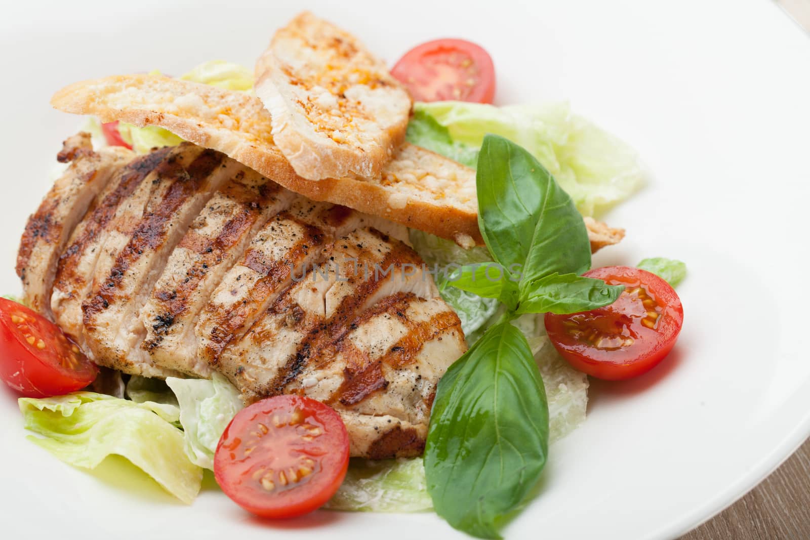 Gourmet delicious caesar salad with grilled beef meat fillet, romaine lettuce, cherry tomatoes,  cheese croutons and basil served in white plate