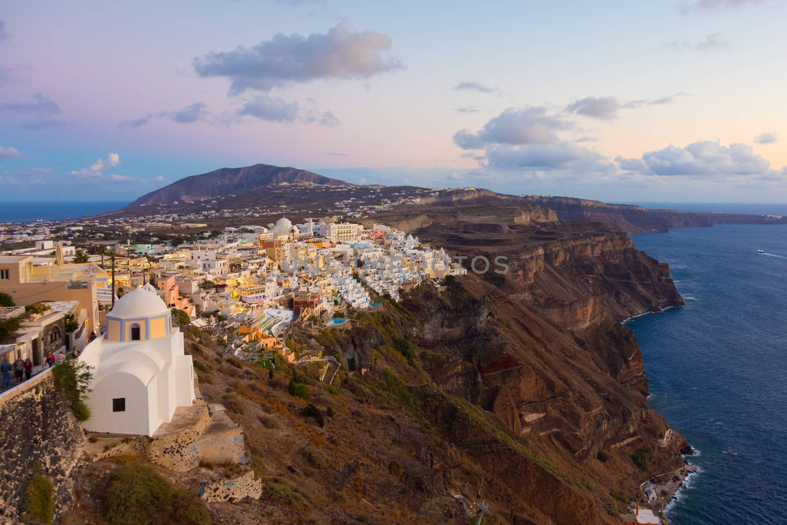 Cityscape of Fira, dramatically located on the edge of the caldera cliff on the island of Thira known as Santorini, Greece. Panorama shot at dusk.