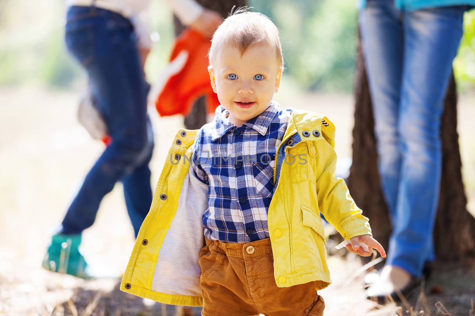 Toddler boy on bright autumn day, with blurred adults in the background