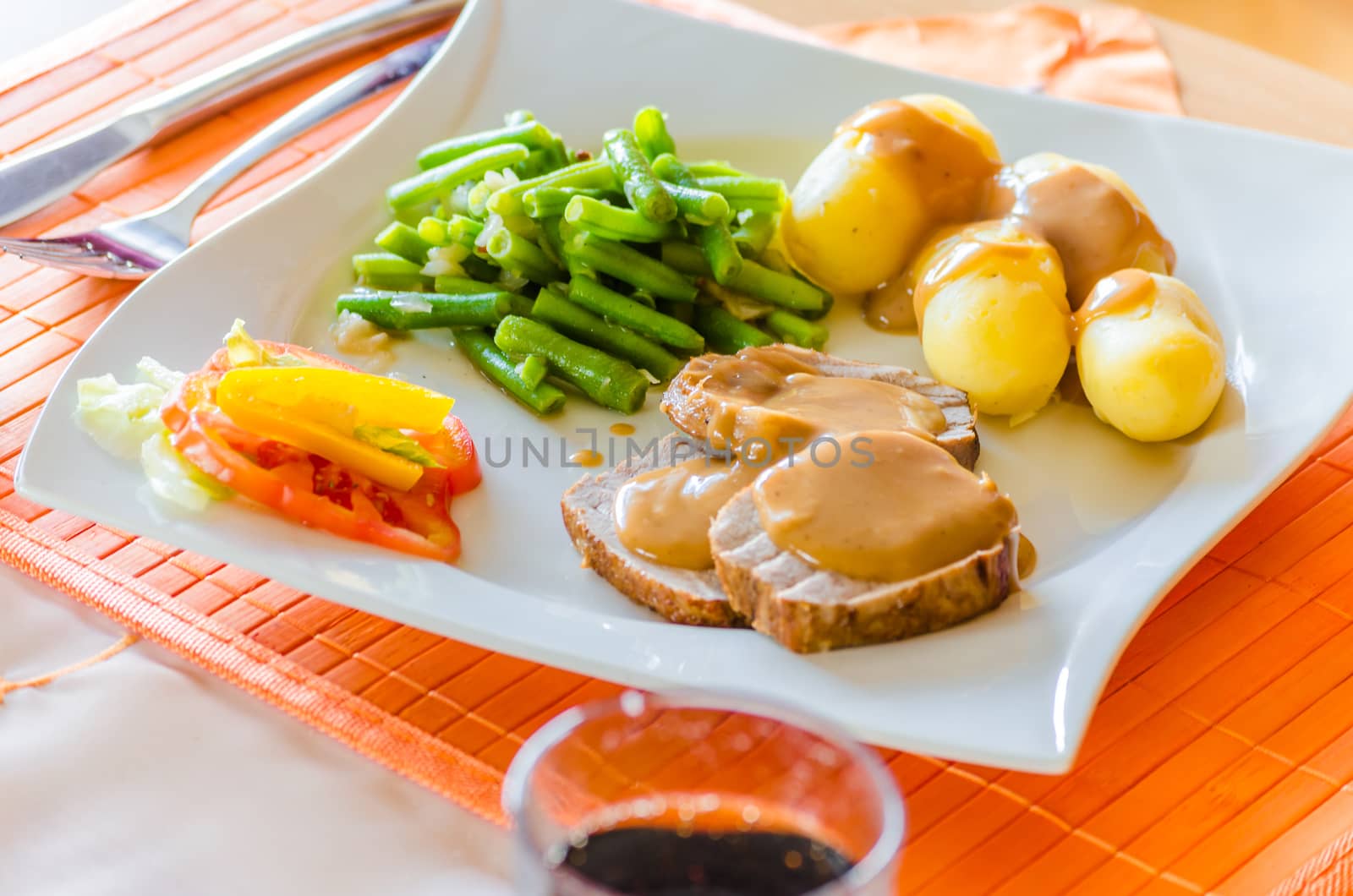 Roast pork, potatoes with sauce on white plate.
