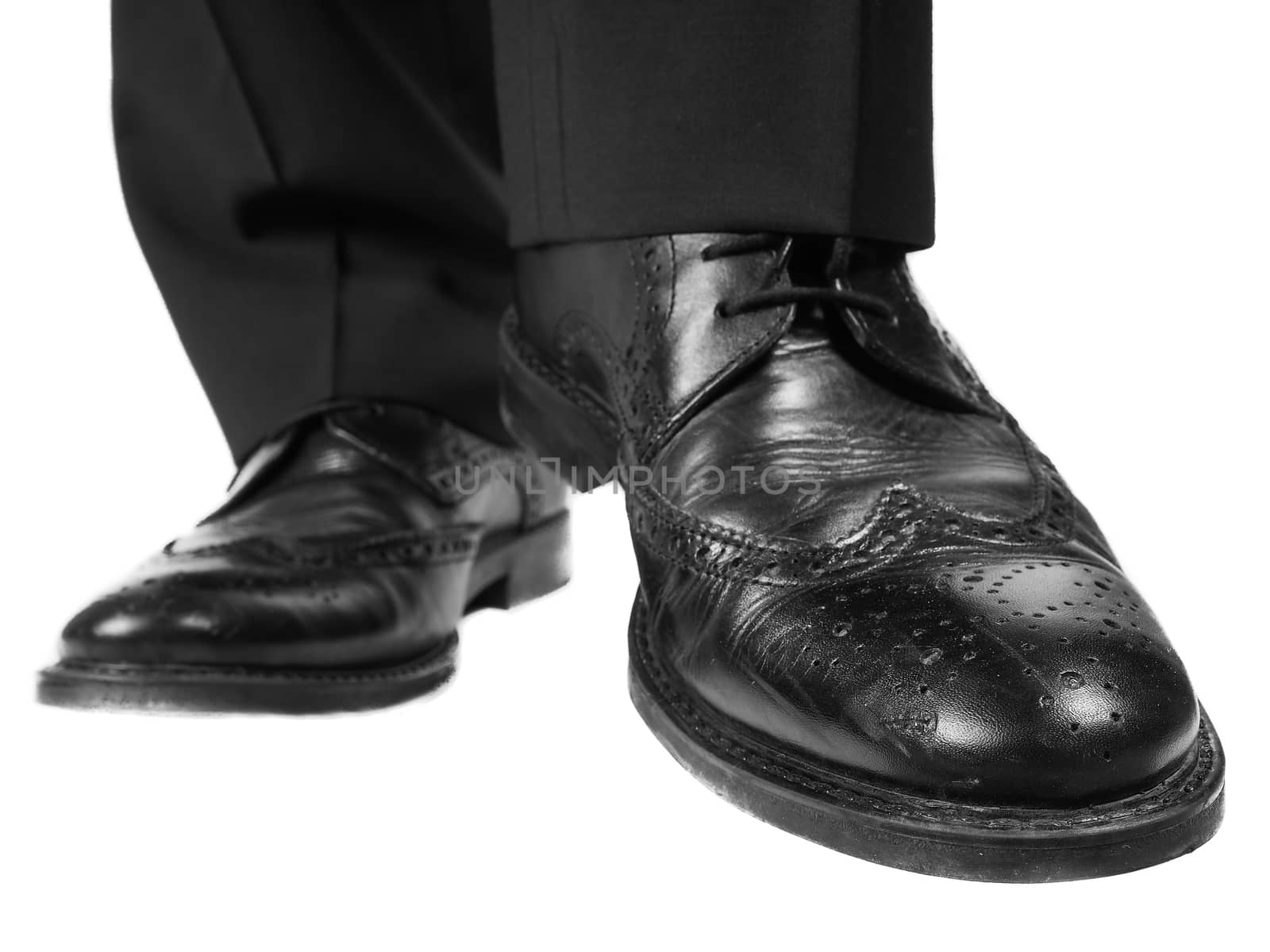 Male person in black suit and leather shoes lifting one shiny shoe towards white