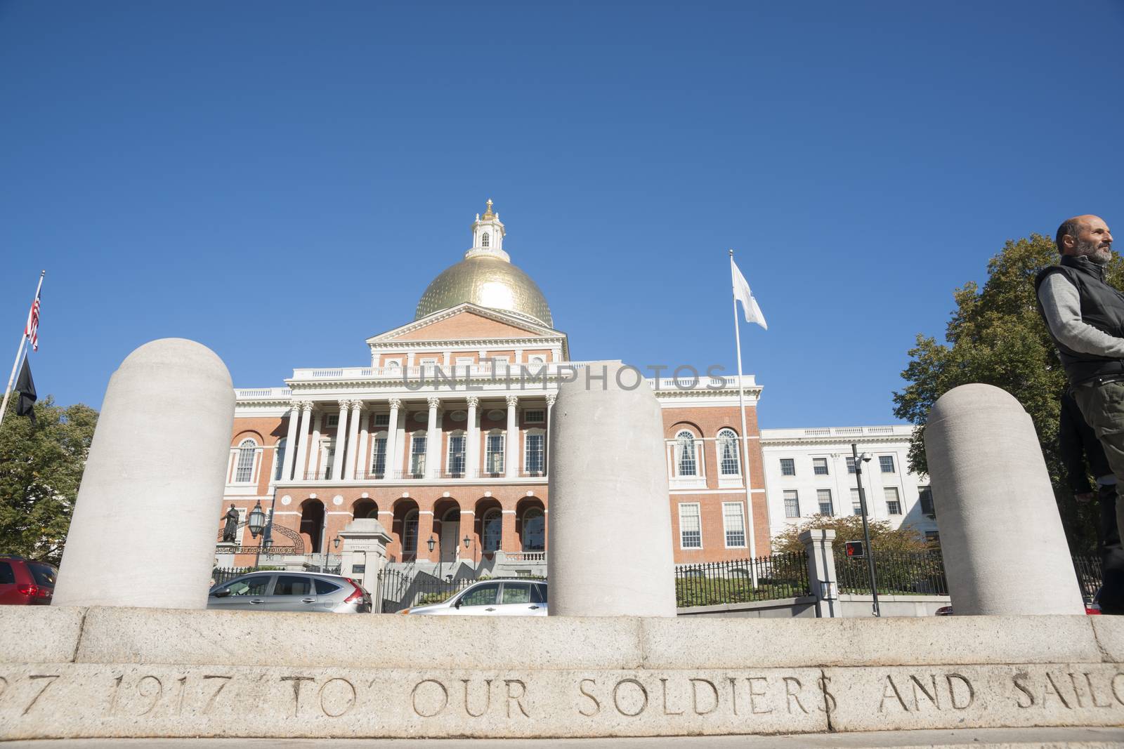 Massachusetts State House is the state capitol and house of government of the state of Massachusetts from memorial steps across road as man walk past.