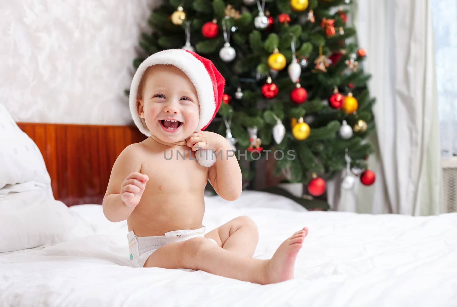 Christmas baby in santa hat sitting on bed by photobac