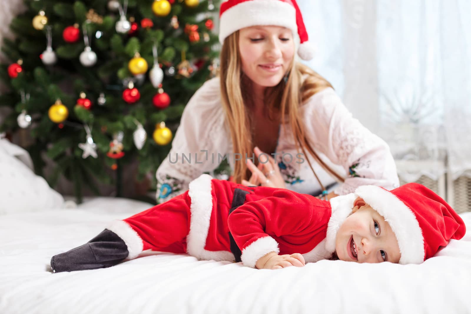 Mother playing with baby dressed in Santa costume by photobac