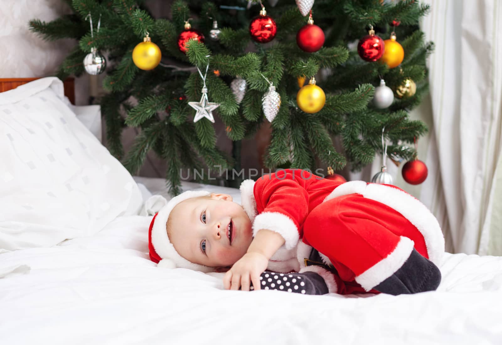 Cheerful little boy in Santa costume lying on bed