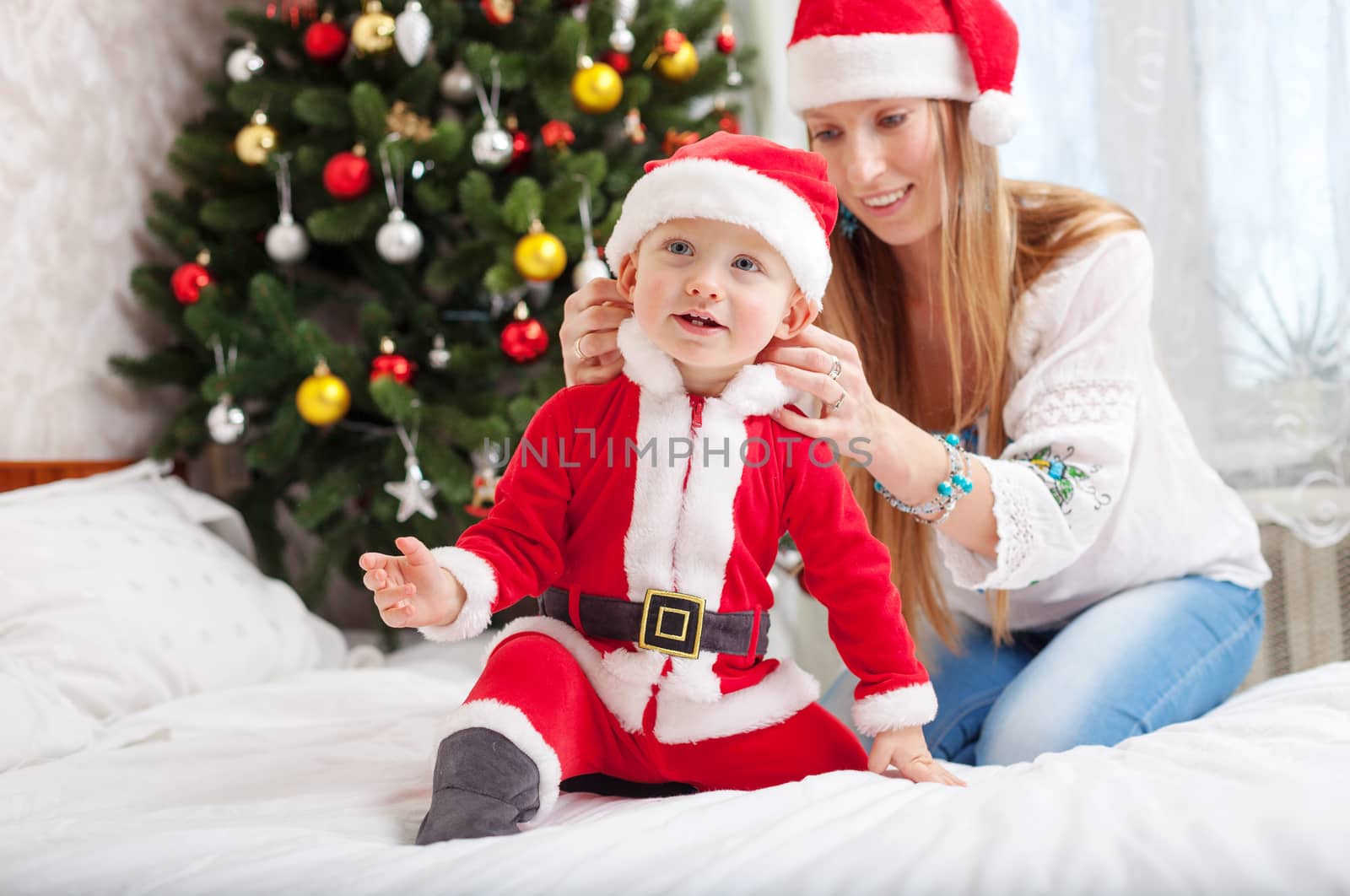 Happy mother putting Santa costume on toddler son by photobac