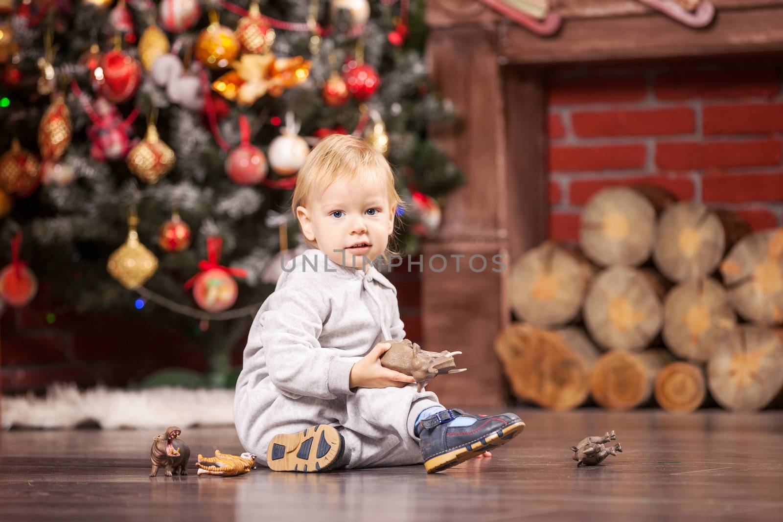 Cheerful little boy playing with his toy animals by Christmas tree