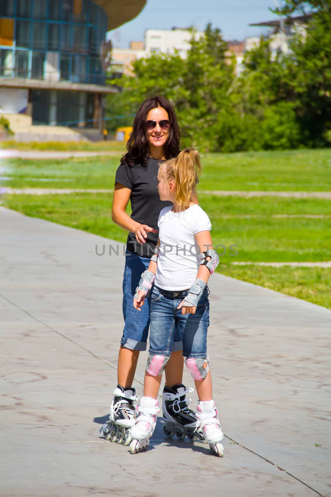 Learning mother and daughter on roller skates in summer