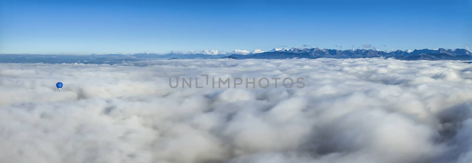 Hot air balloon upon clouds seeing Alps mountains range and deep blue sky, Switzerland