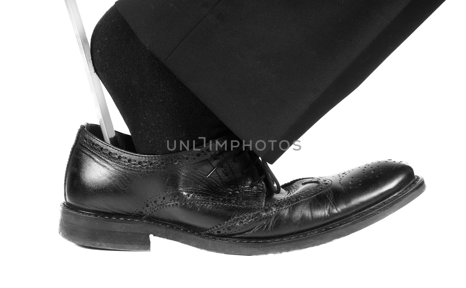 Person wearing black suit and socks entering foot into black leather shoe with shoehorn towards white