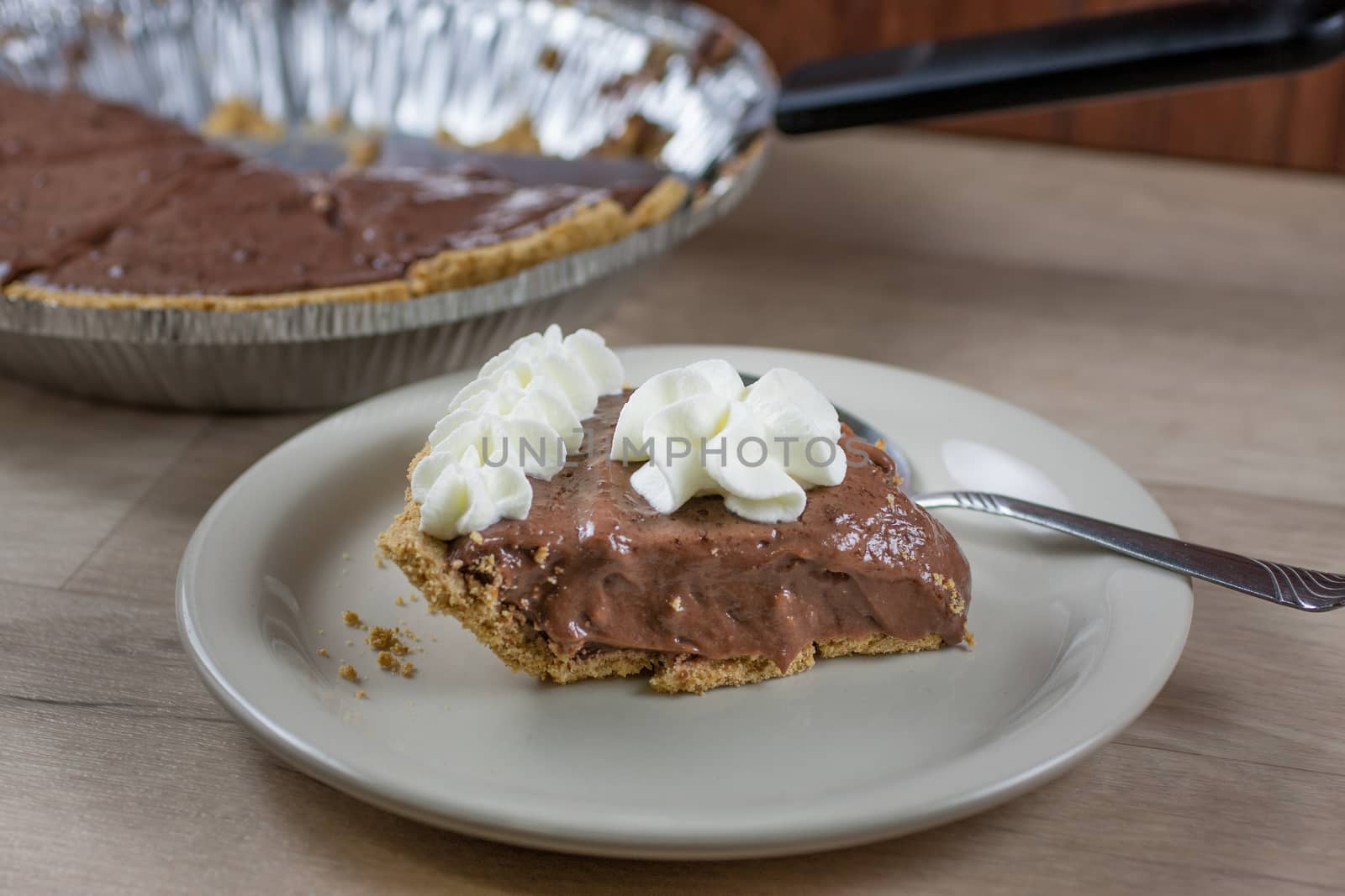 Chocolate cream pie on a white plate with the rmaining pie in the background.