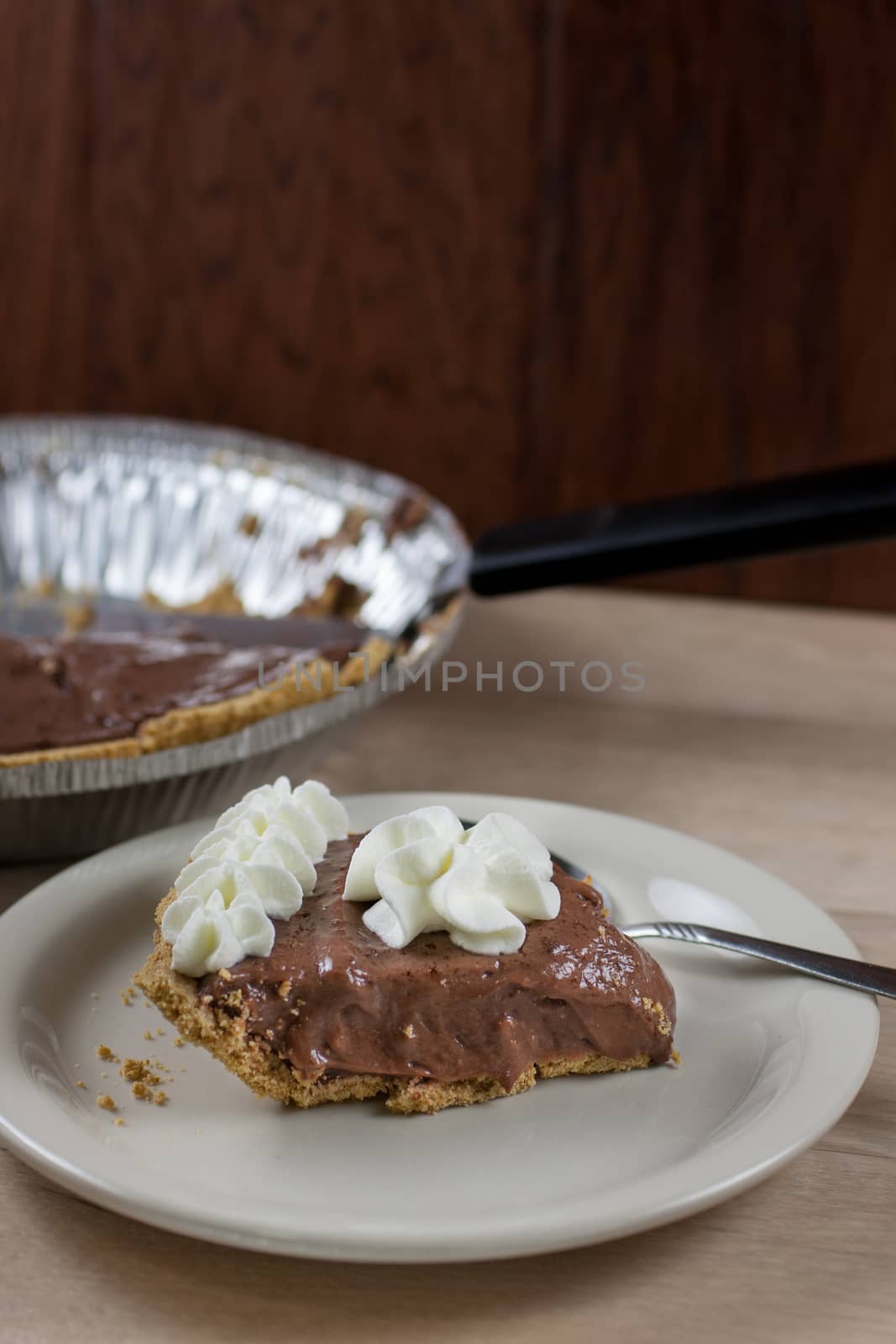 Chocolate cream pie on a white plate with the rmaining pie in the background.