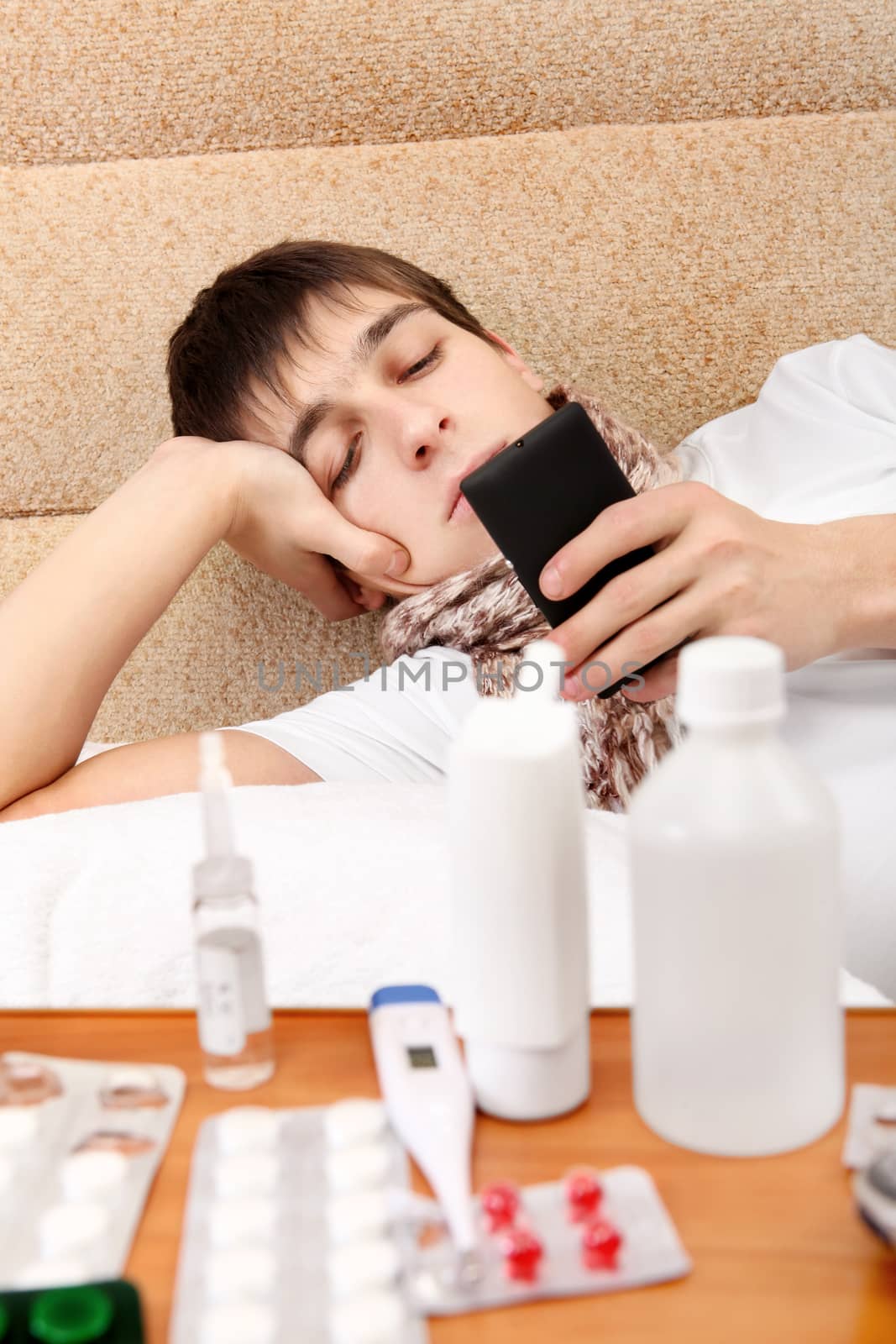 Sick Teenager with Cellphone on the Sofa at the Home with Pills on foreground