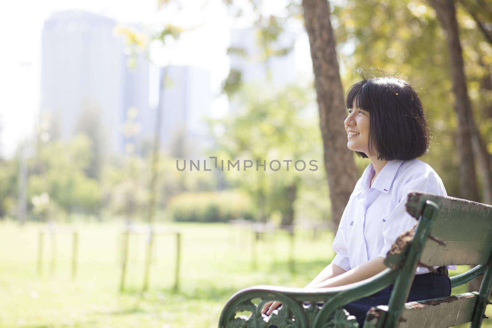 Schoolgirl sitting on the bench. Within the park. Girl smiling