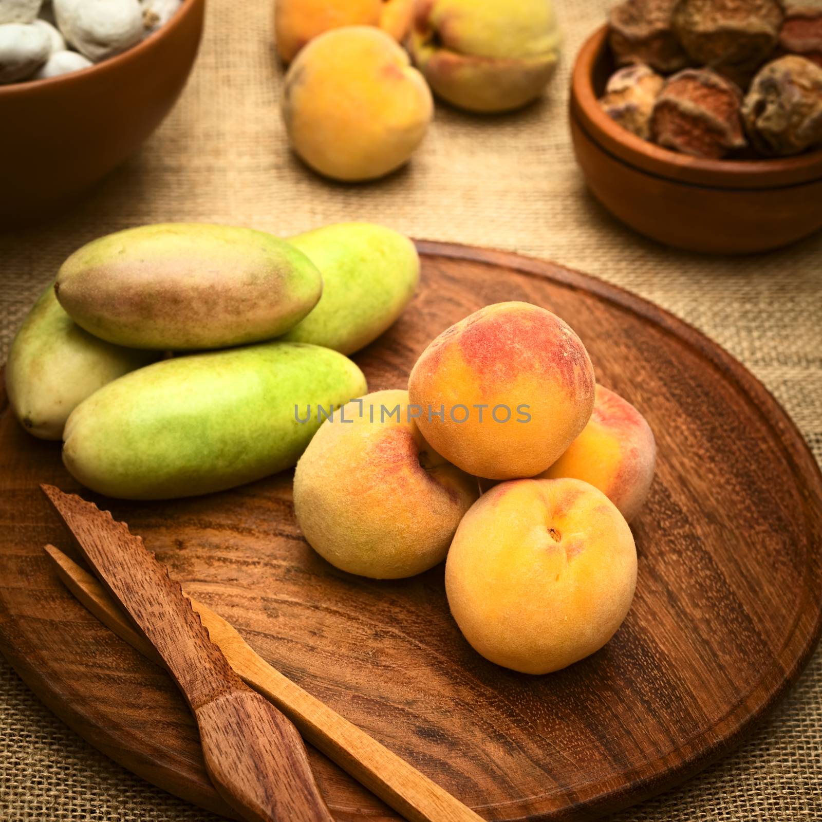 Peaches on round wooden plate with banana passionfruit (lat. Passiflora tripartita) next to it, photographed with natural light (Selective Focus, Focus on the front of the peaches)