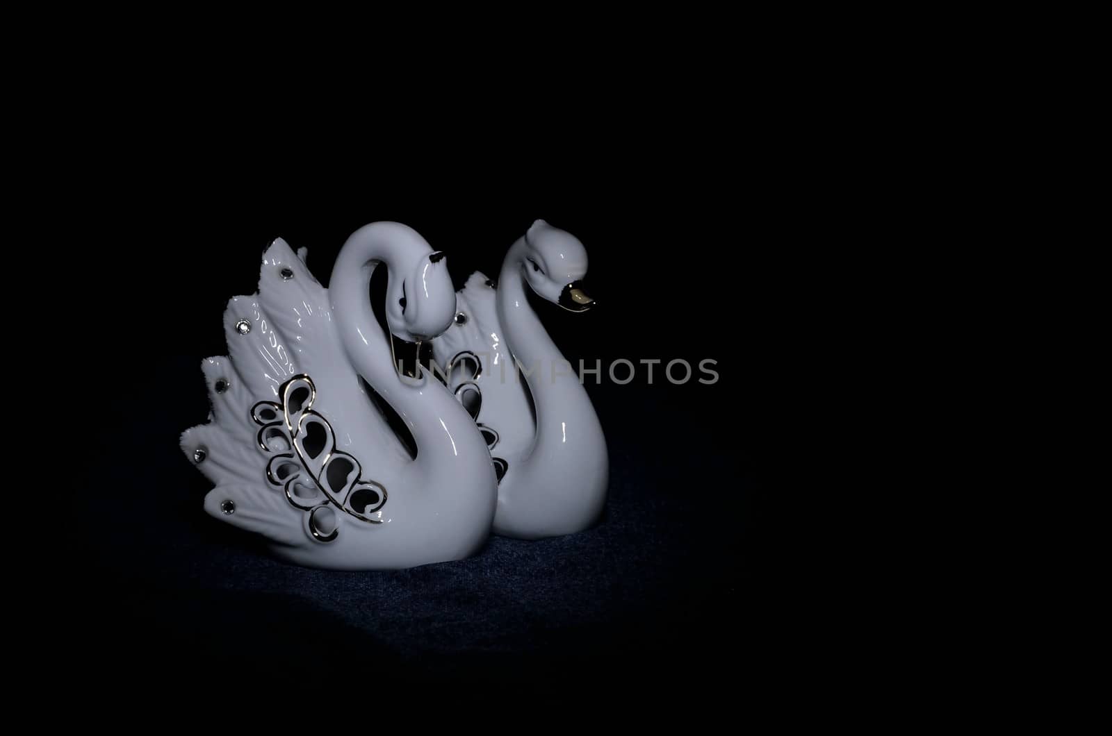 Photo of two ceramic figures of swans on a dark background.