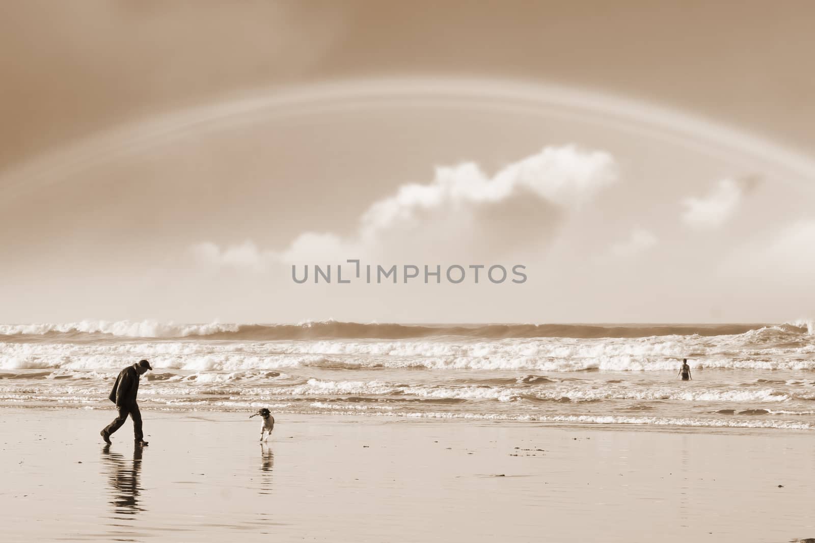 one man and his dog on Ballybunion beach county Kerry Ireland with a rainbow in sepia