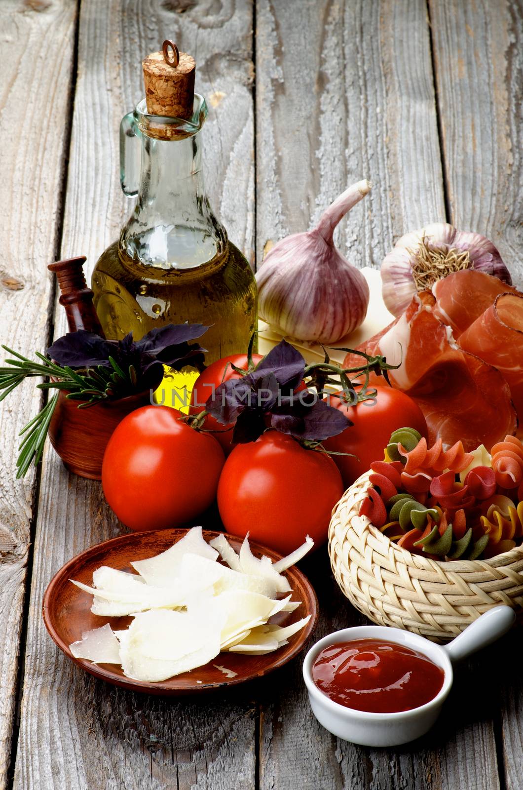 Arrangement of Raw Rotini Pasta with Tomatoes, Spices, Smoked Ham, Olive Oil and Grated Cheese isolated on Rustic Wooden background