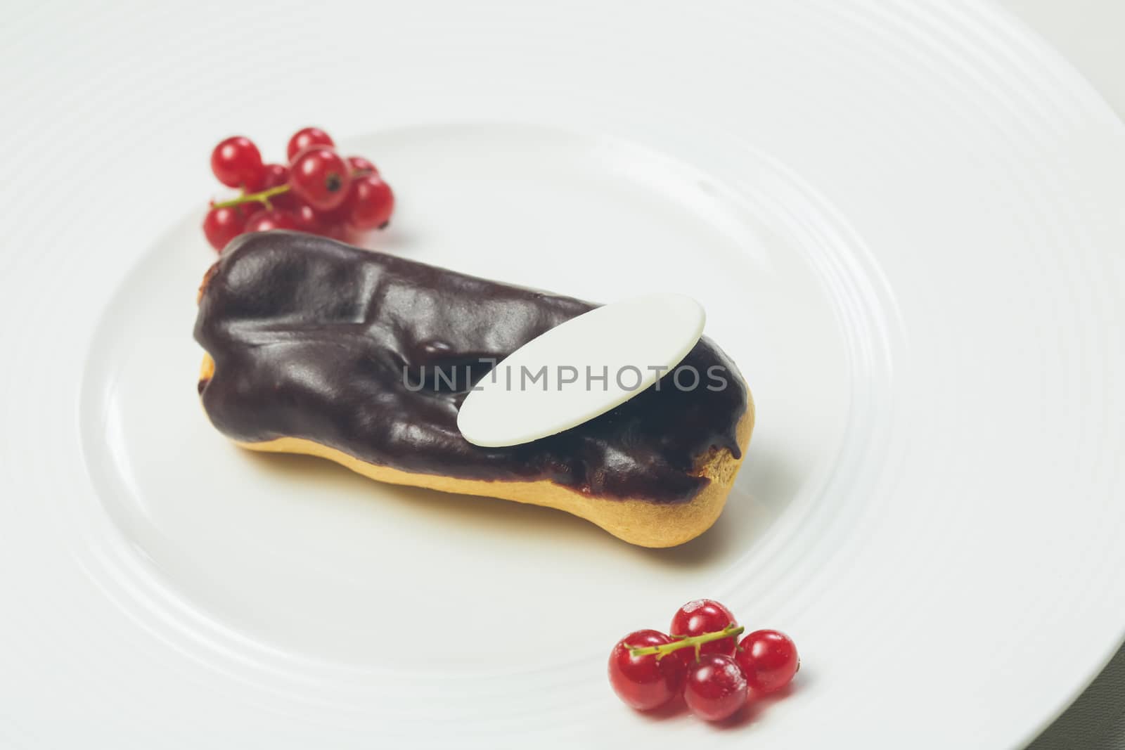 Single chocolate eclair with space for text on white  plate. Warm colors. Shallow dof. 