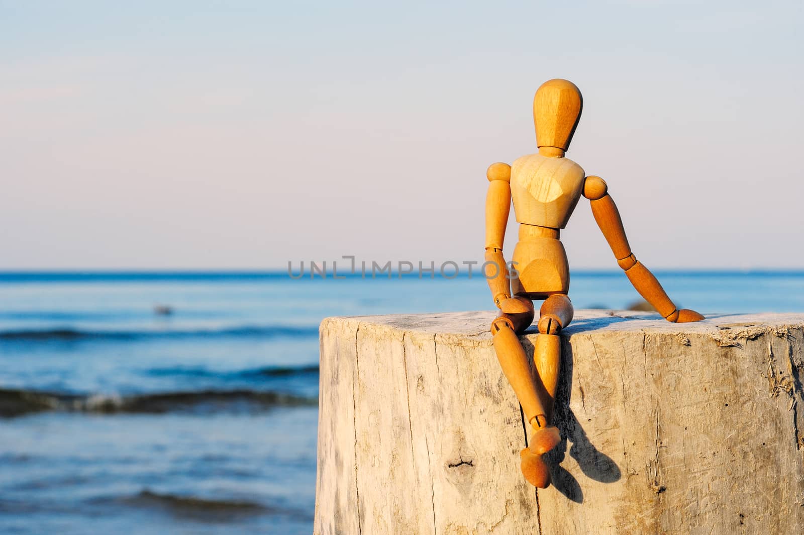 Figurine of wooden woman sitting on the stone at the sea