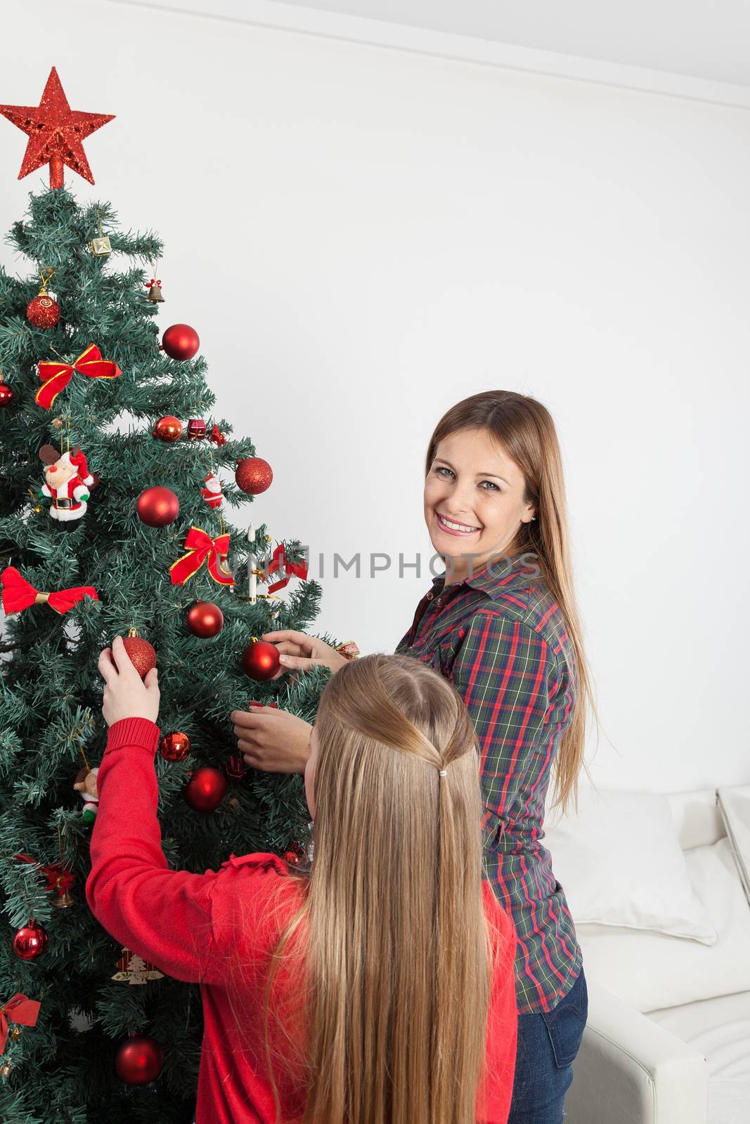 Happy woman decorating the christmas tree with her daughter by ifilms