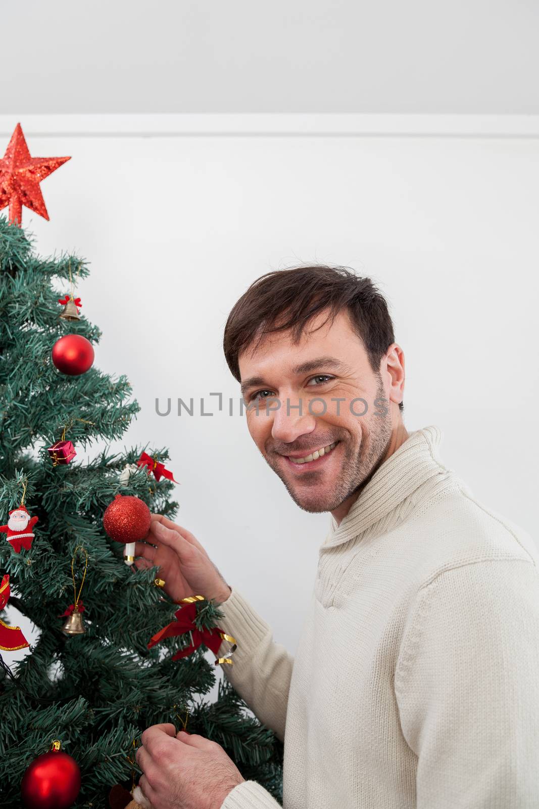 30-35, adult, artificial, background, balls, brown, caucasian, celebration, christmas, decorating, decorations, eyes, festive, garland, green, handsome, happy, holiday, male, man, men, model, old, ornaments, person, pine, pleasure, property, red, releases, santa, seasonal, smiling, sweater, tall, tradition, tree, vertical, white, winter, xmas, years, young, look, looking, camera, smile