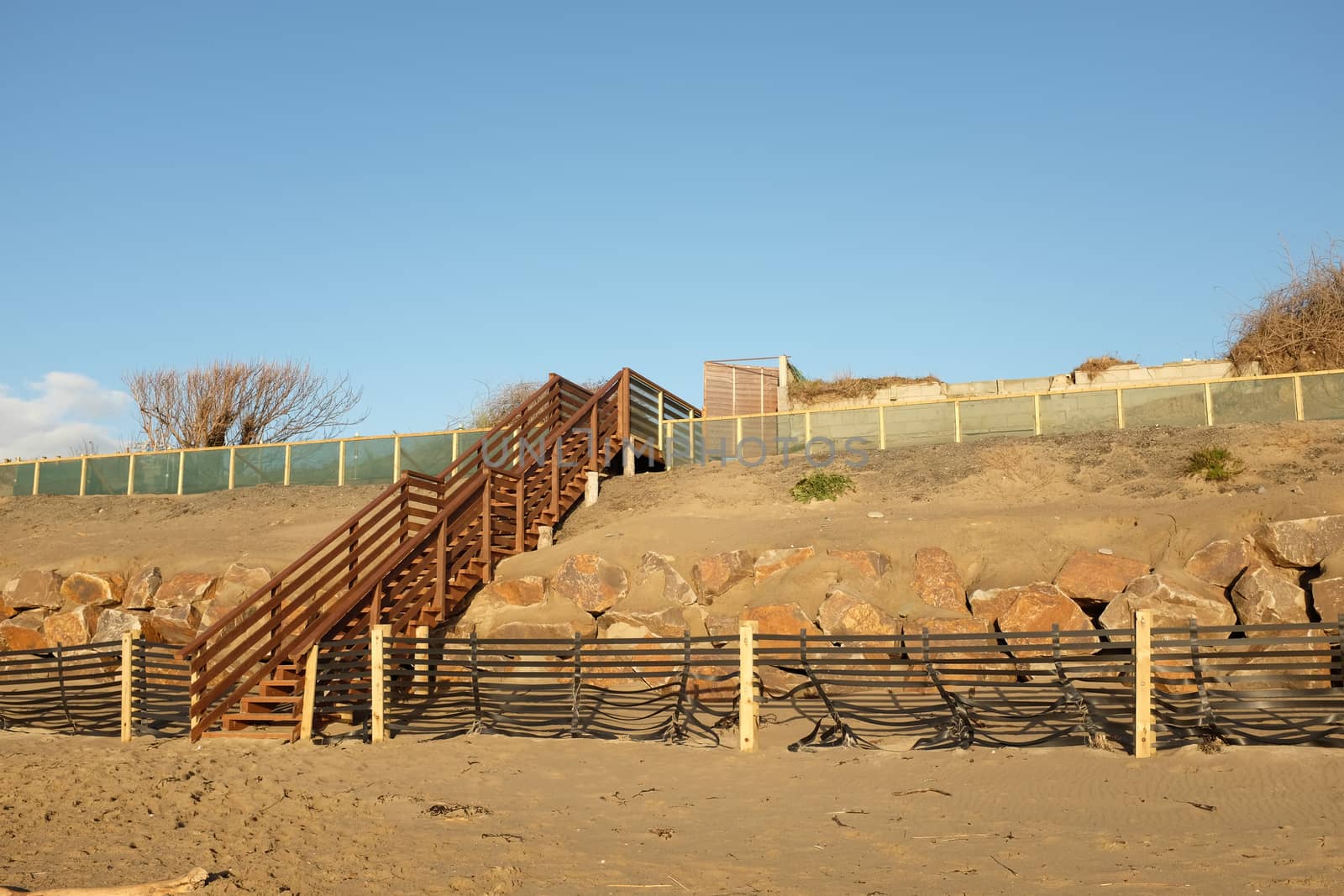 A set of wooden stairs, steps, built over a constructed dune with sand drift fence, base rock and overlayed sand.
