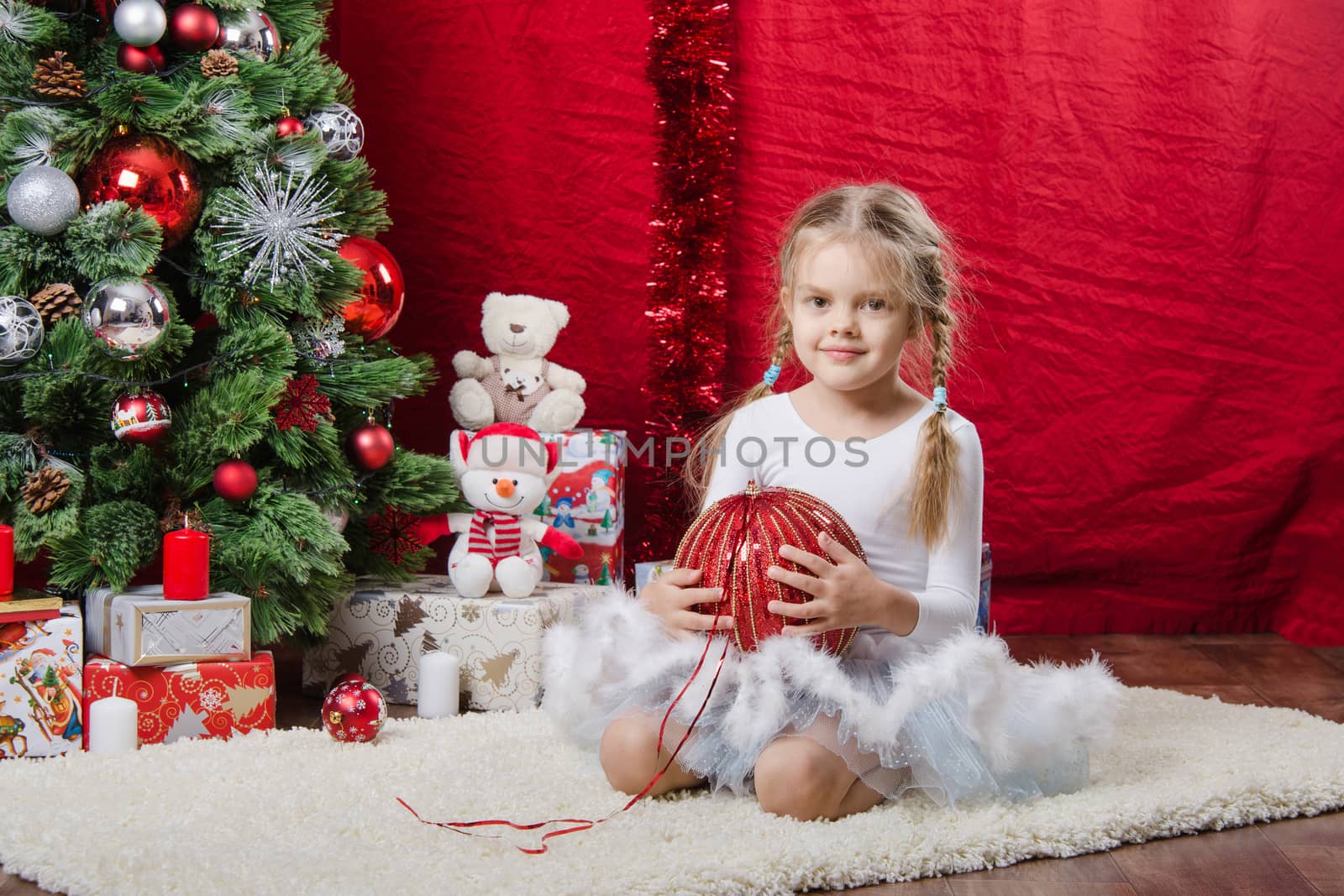Girl sitting on a rug in the Christmas tree with Christmas tree balls