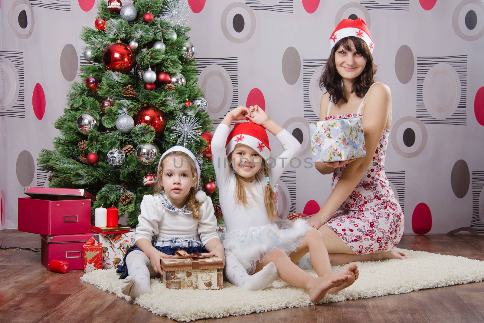 Mom and two daughters sitting on a rug in the Christmas tree