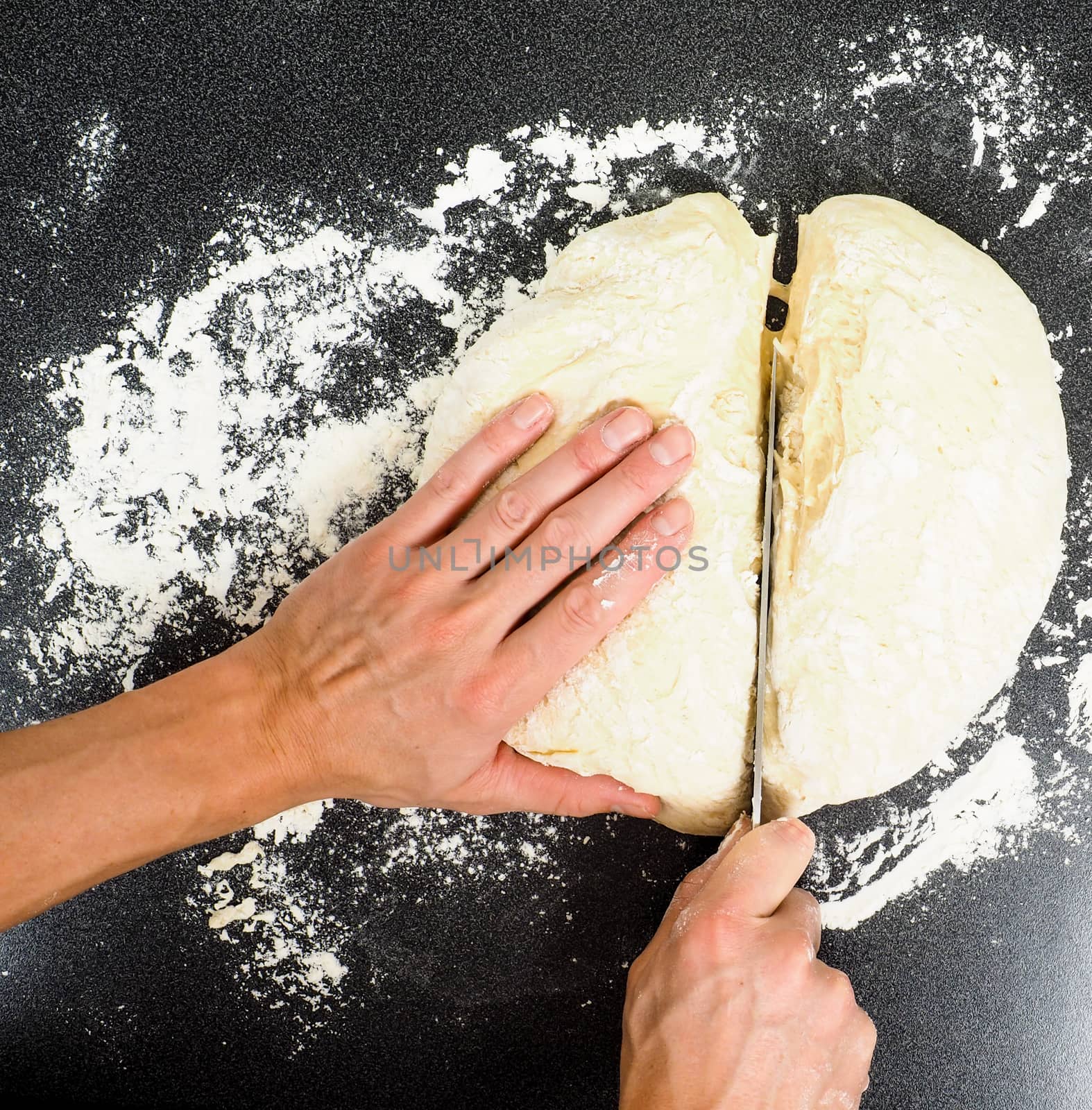 Hands cutting a lump of dough into two pieaces on black table with flour spread