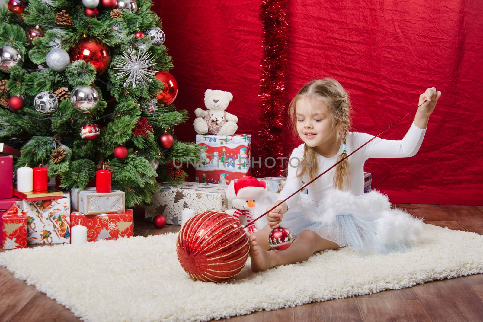Girl sitting on a rug in the Christmas tree with Christmas tree balls