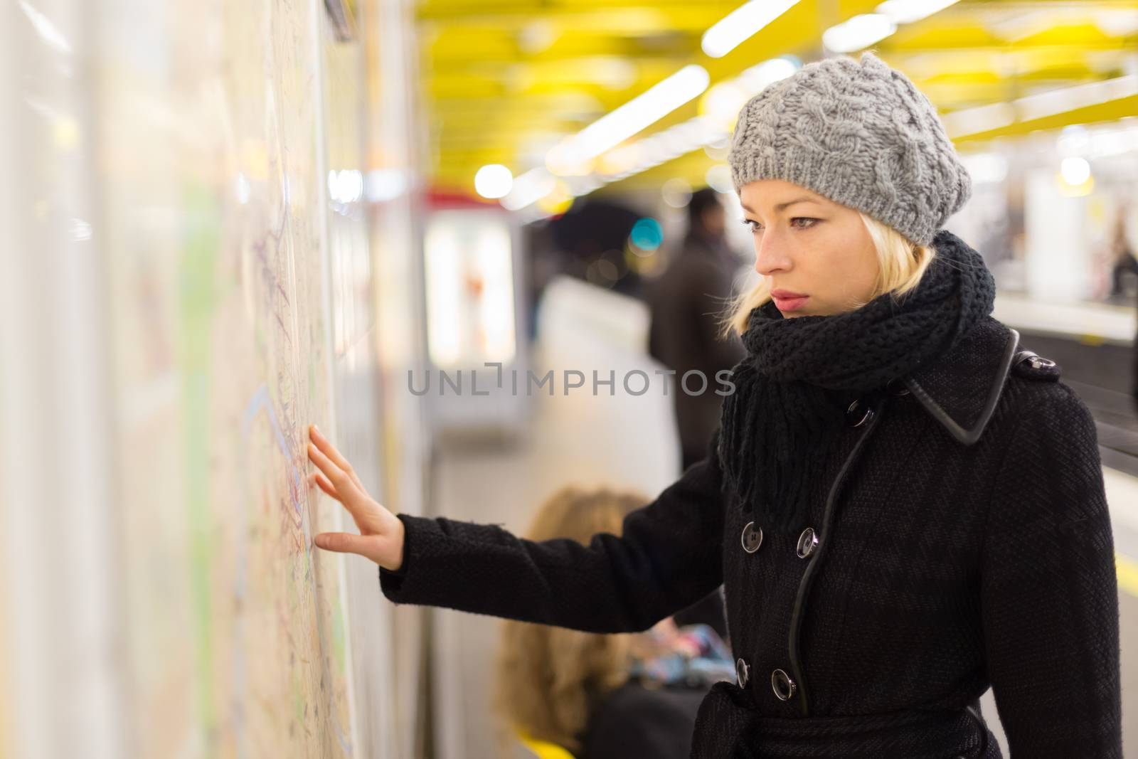 Casually dressed woman wearing winter coat, orientating herself with public transport map panel, pointing on her final destination. Urban transport.