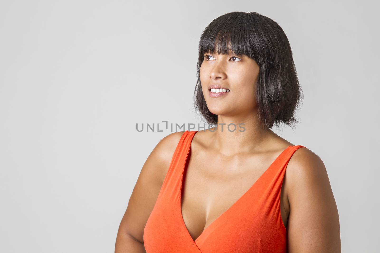 Twenty something filipino woman, wearing an orange low cut dress looking to the left