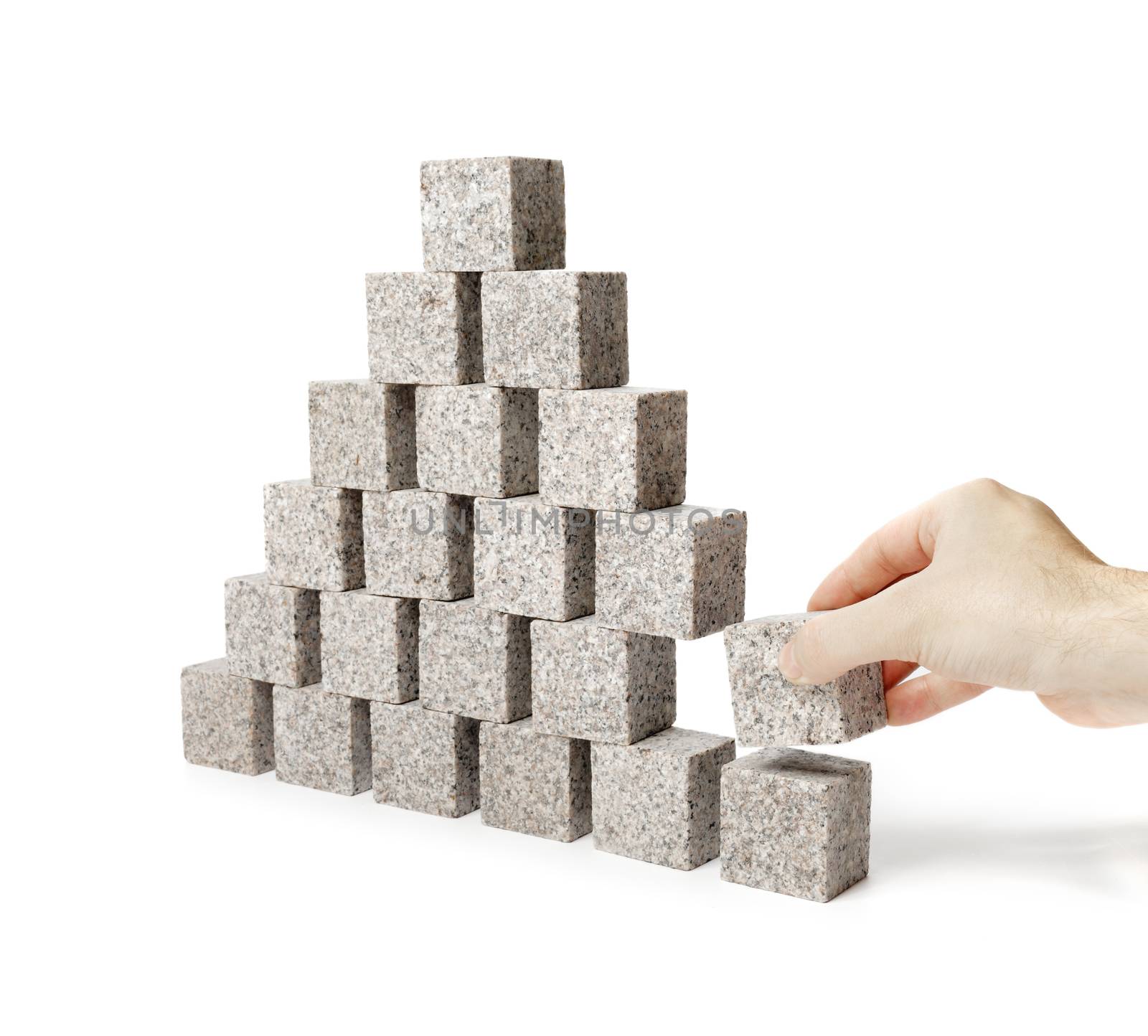 Hand removing one block of a pyramid made of small granite rock blocks.