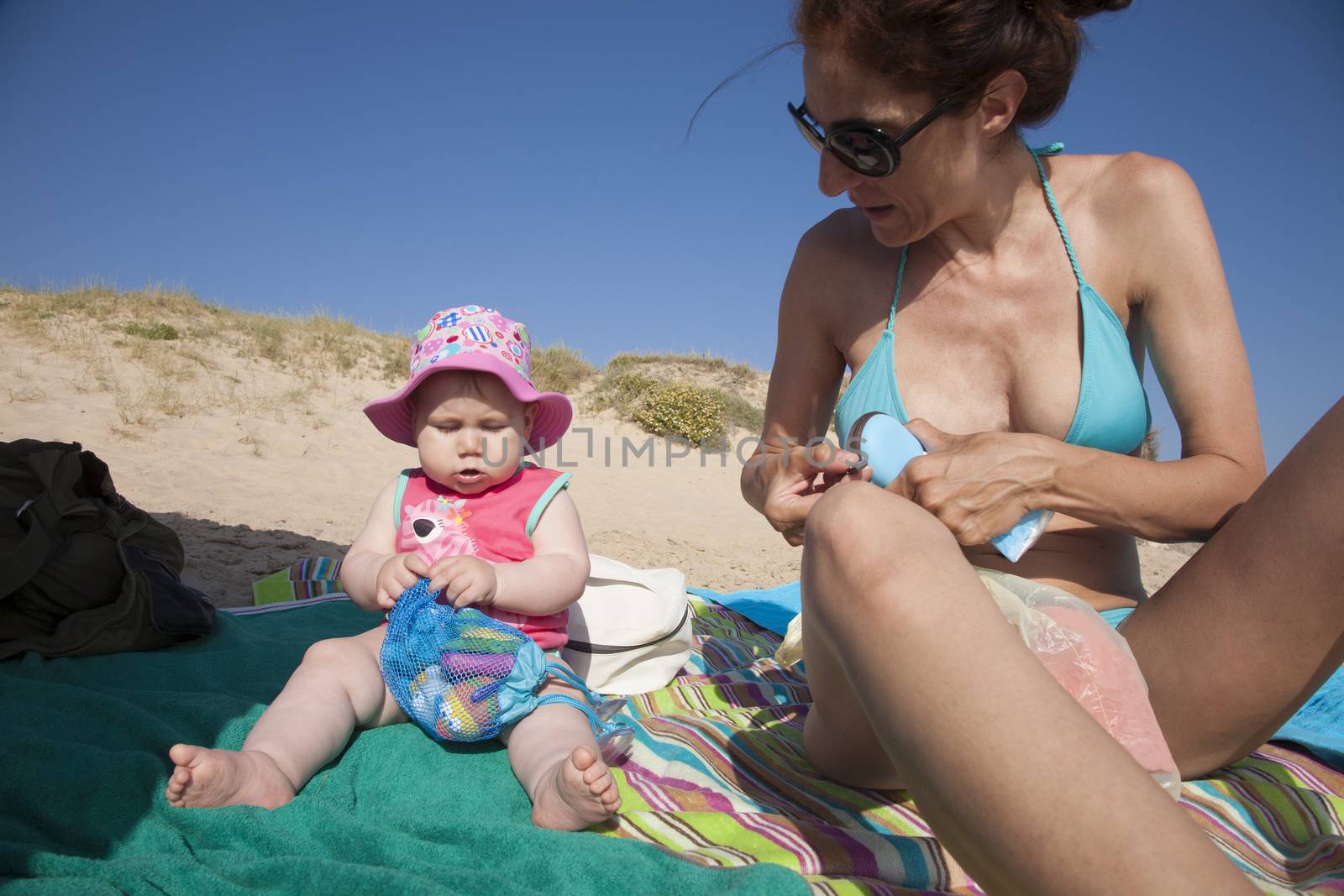 mother and baby sitting on towels at beach