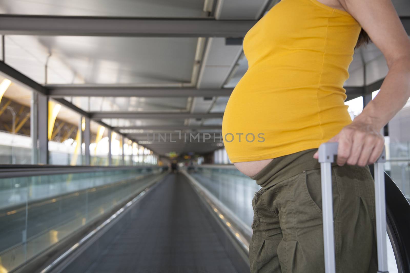 tummy of woman pregnant pulling suitcase in airport hall