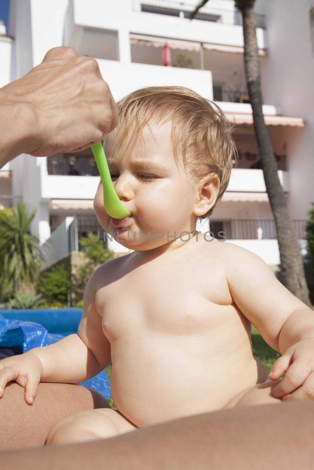 naked baby eating from green spoon in mom hand