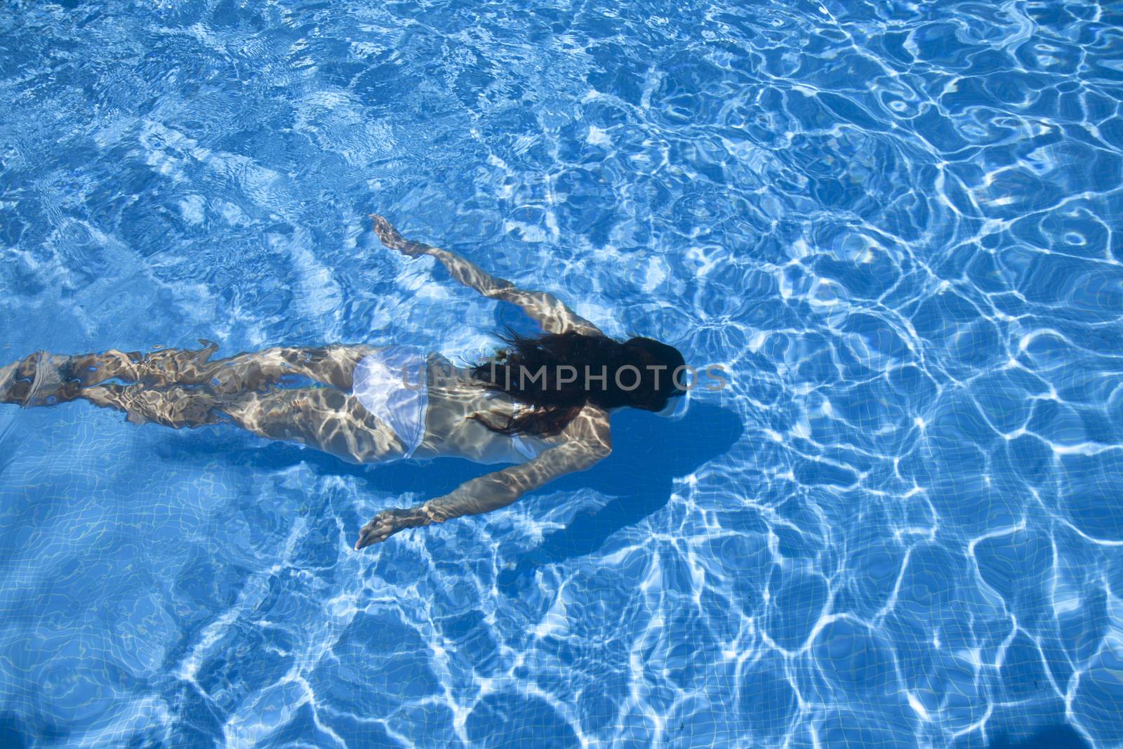 woman with white bikini diving at the bottom of a blue pool