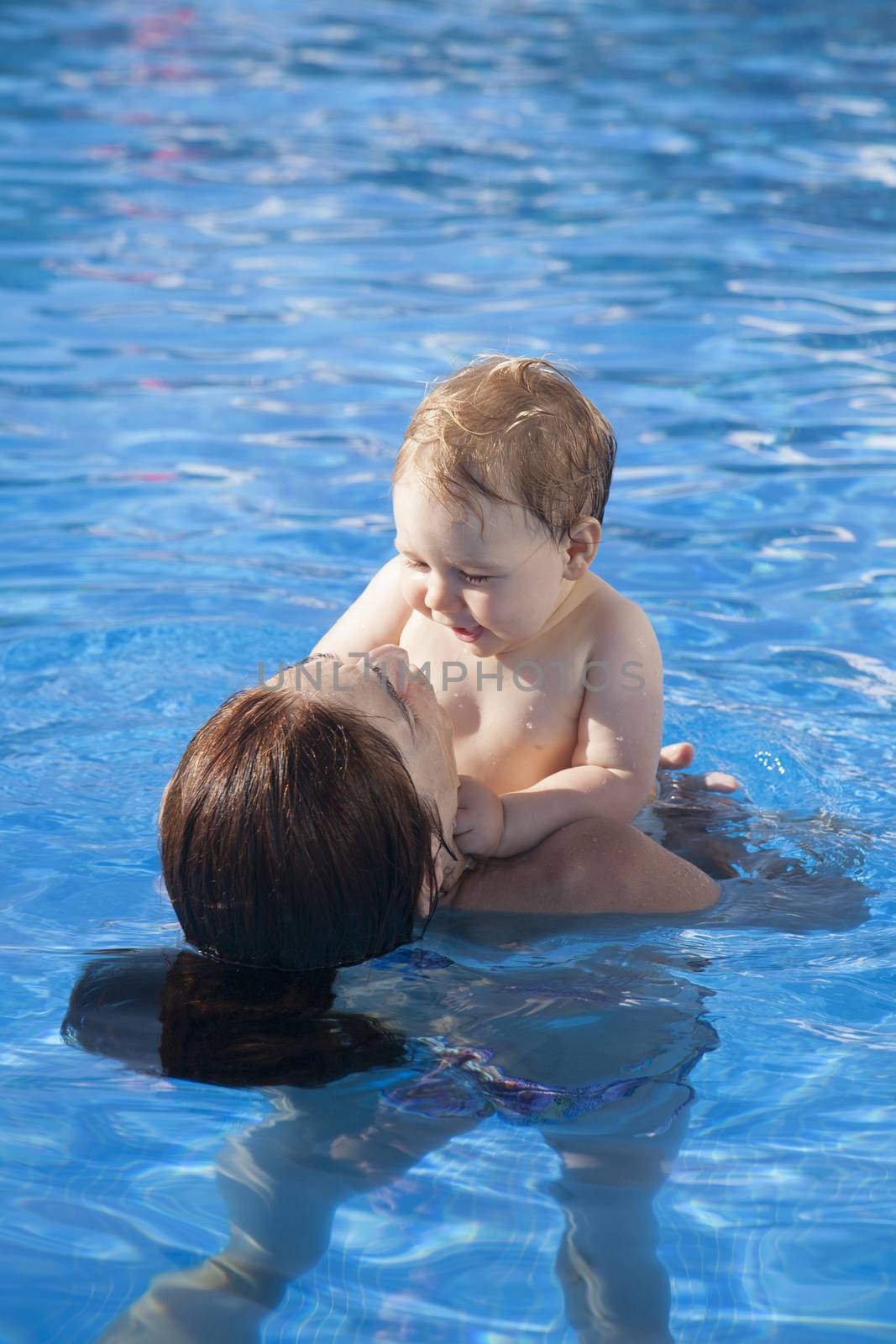 mother and baby in swimming pool embraced looking themselves