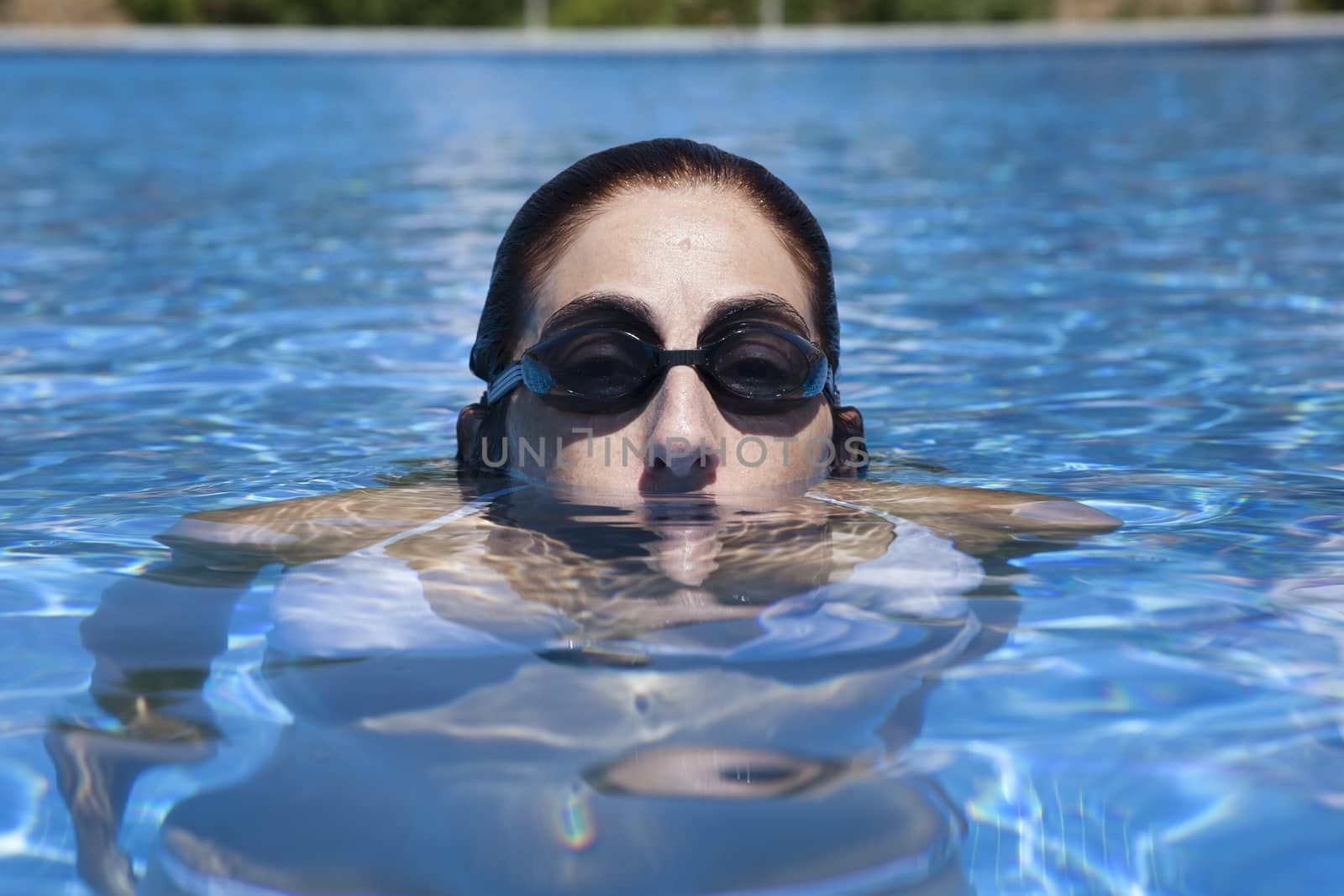 woman with black goggles peering out of water in a blue pool