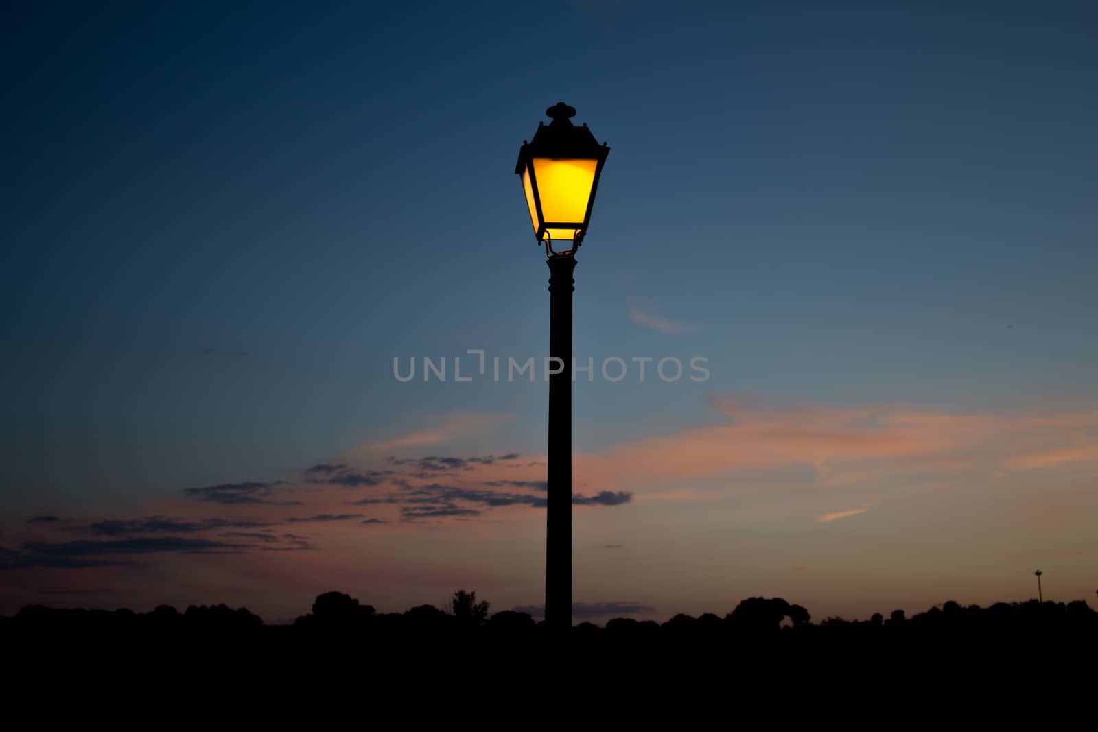 The streetlamp iluminates the country side, anticipating the coming night