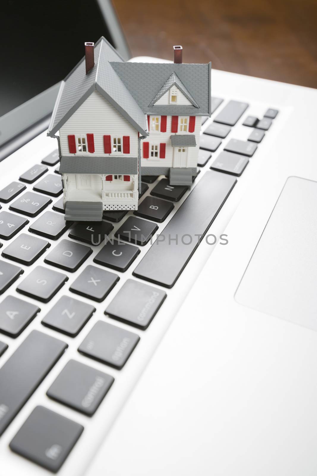 Miniature House And Laptop Computer Resting on Desktop.