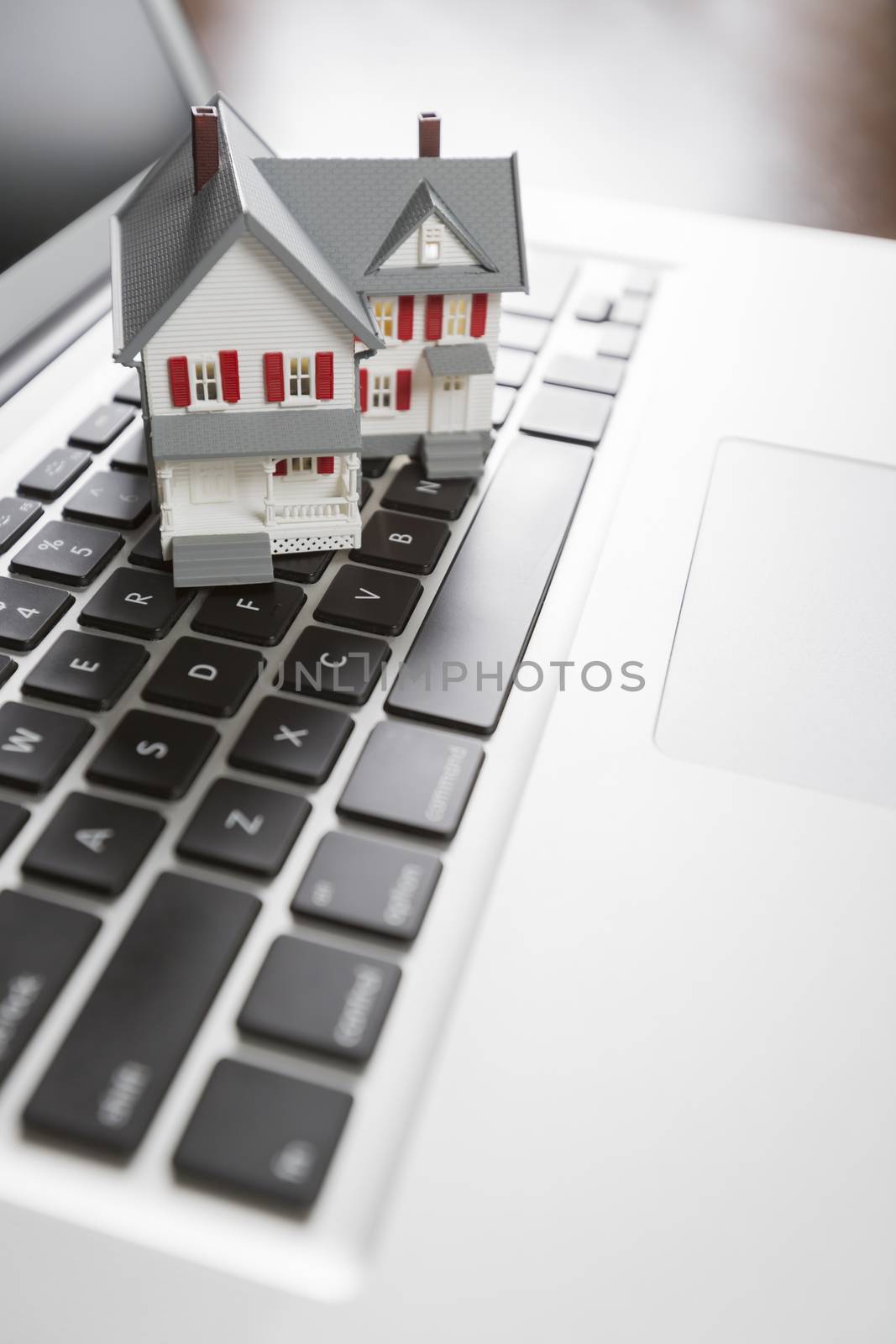 Miniature House And Laptop Computer Resting on Desktop.