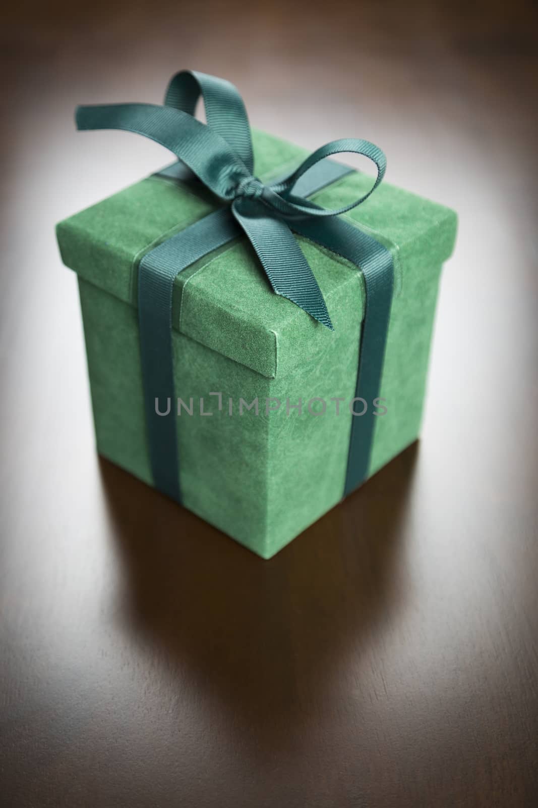 Green Gift Box with Ribbon and Bow Resting on Wood Surface.
