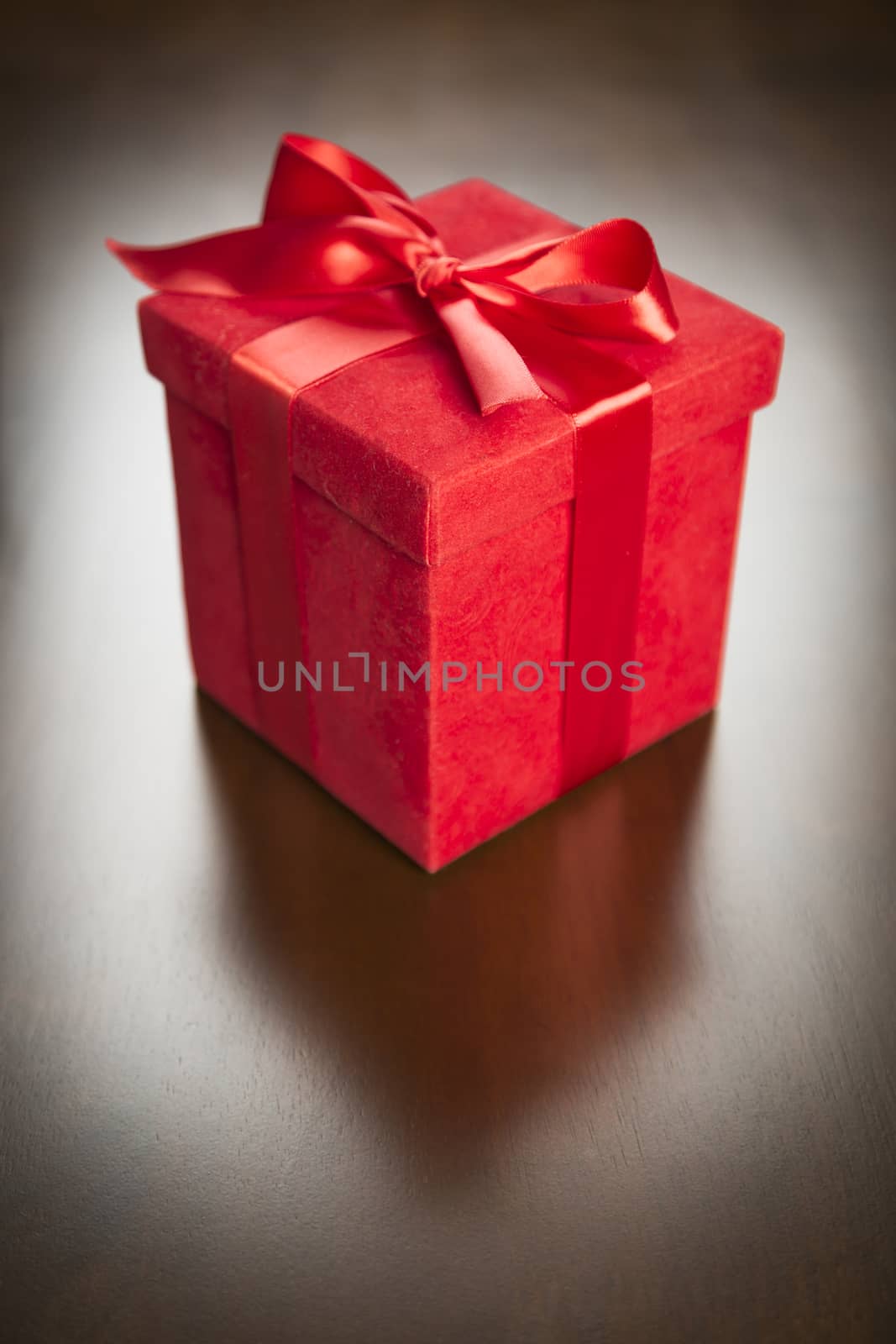 Red Gift Box with Ribbon and Bow Resting on Wood Surface.