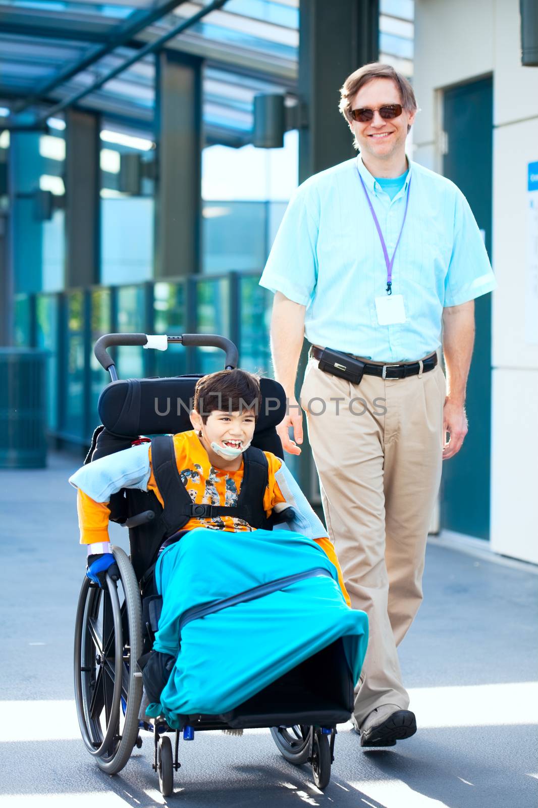 Man walking next to little boy in wheelchair outside medical fac by jarenwicklund