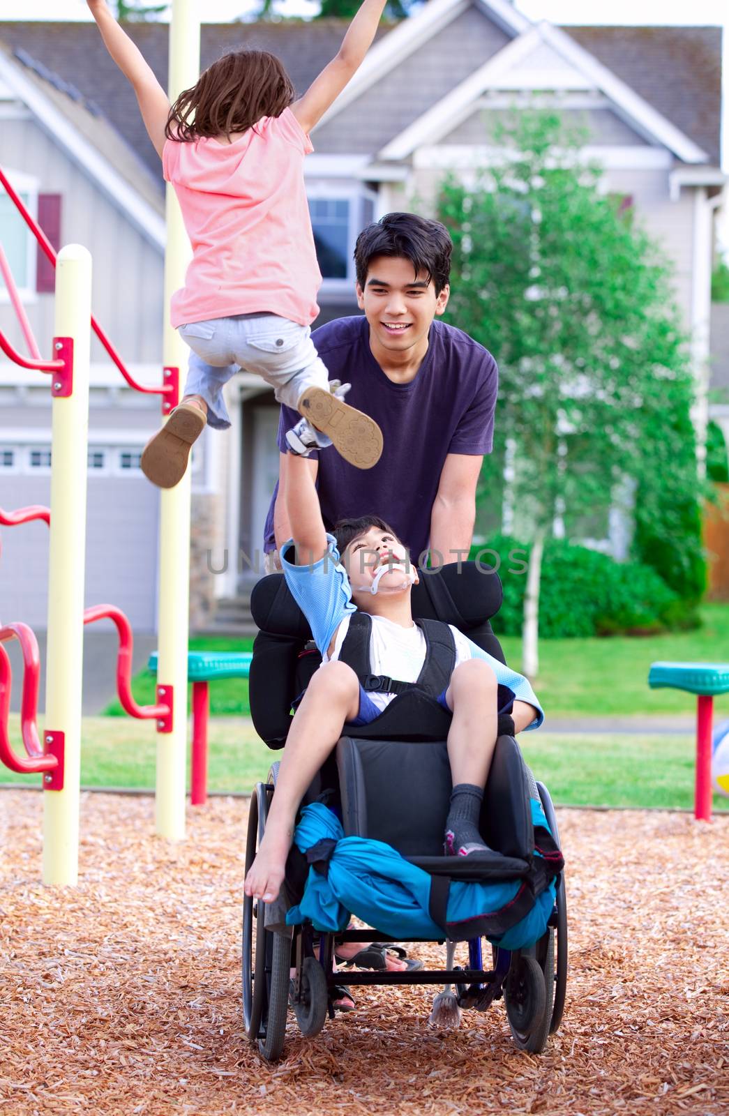 Disabled boy in wheelchair enjoying watching friends play at park on jungle gym