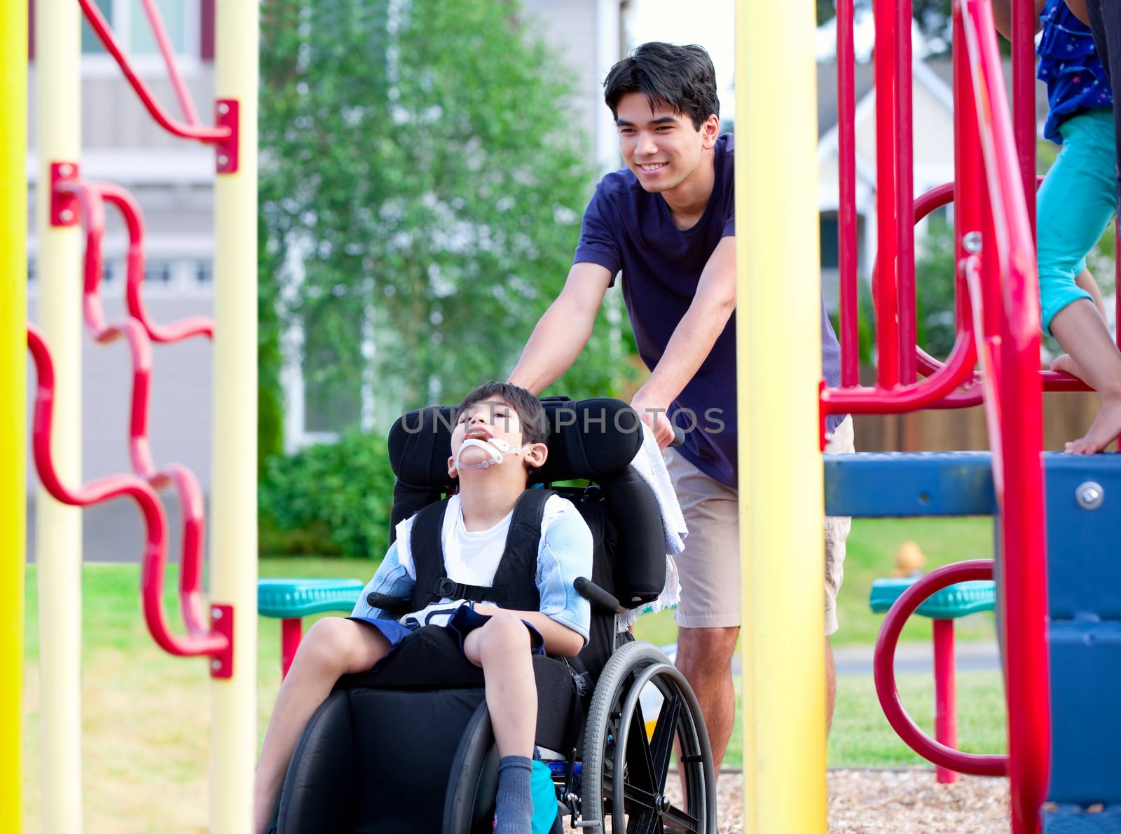 Disabled boy in wheelchair enjoying watching friends play at park on jungle gym
